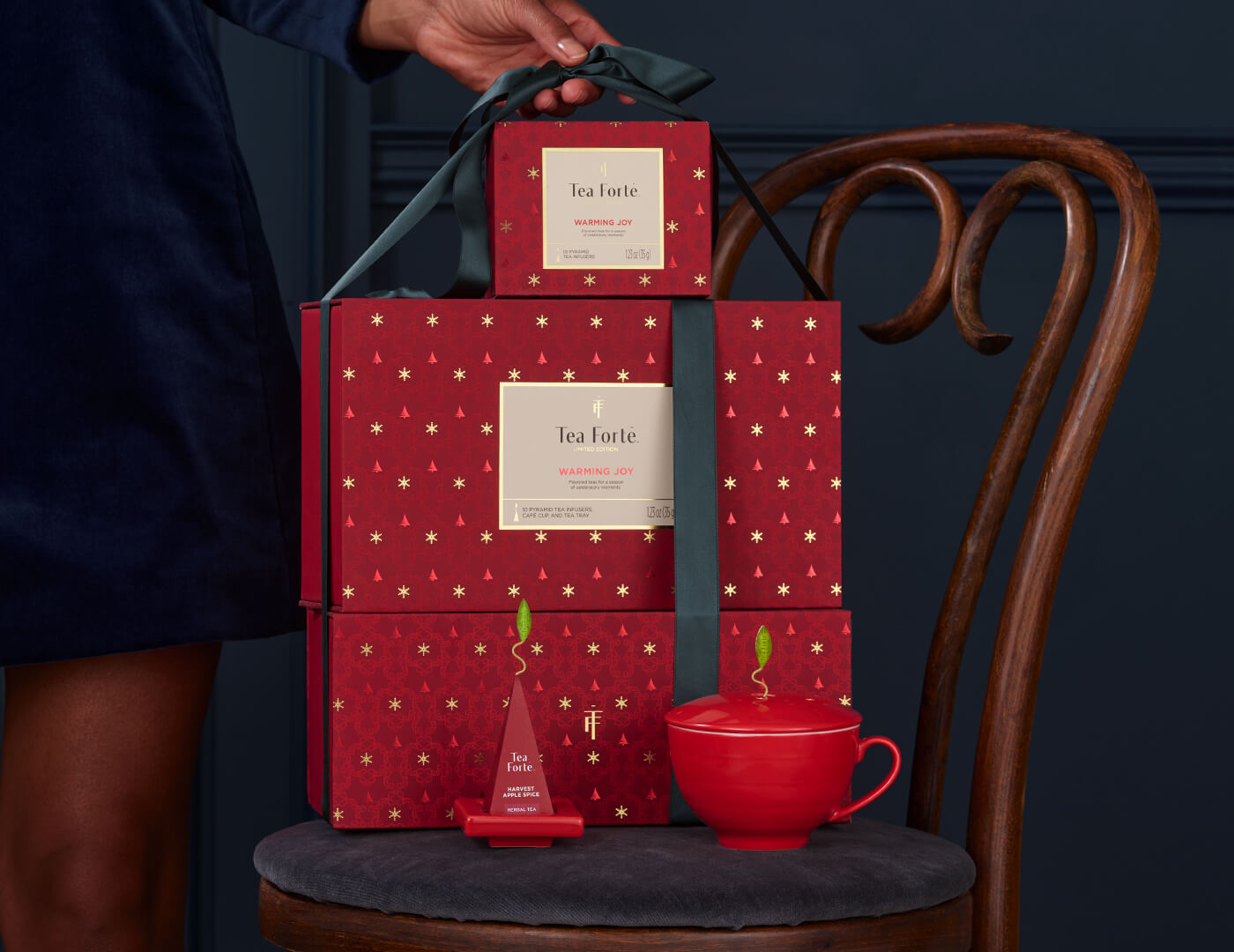 Warming Joy Gift Set wrapped with a ribbon, sitting on a chair with cup and tea tray nearby