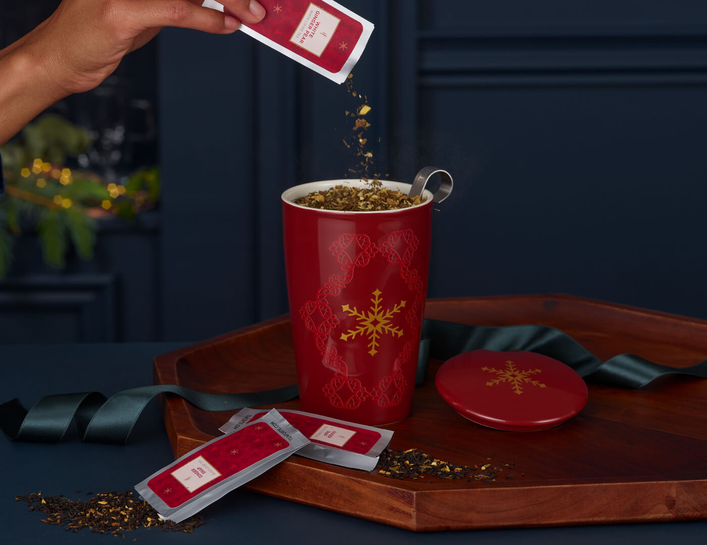 Pouring loose tea into a KATI® Steeping Cup & Infuser Warming Joy, with tea pouches on a wooden tray