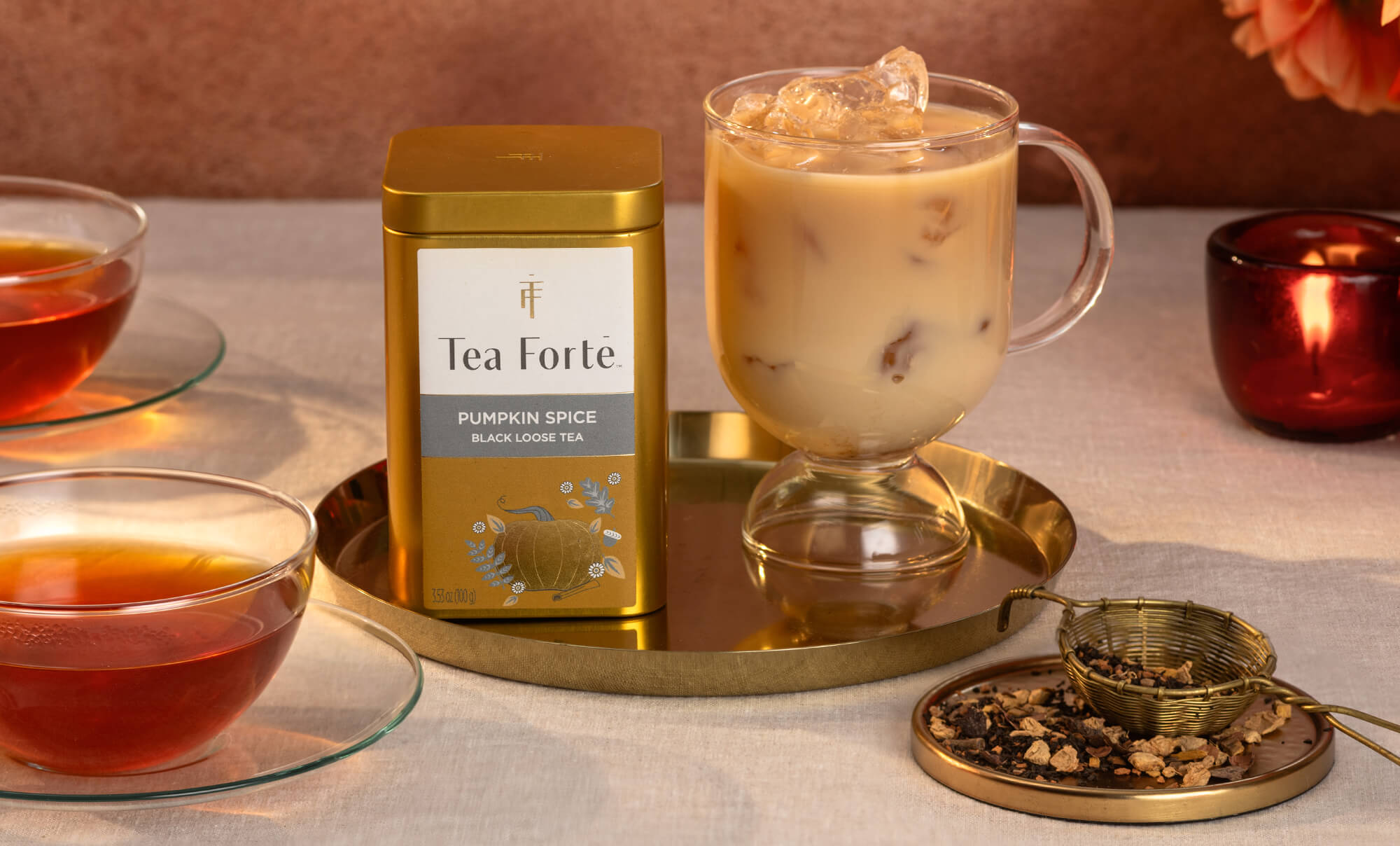Tea Forte pumpkin spice Loose Leaf Tea Canister with a glass of iced tea and tea leaves on a table.

